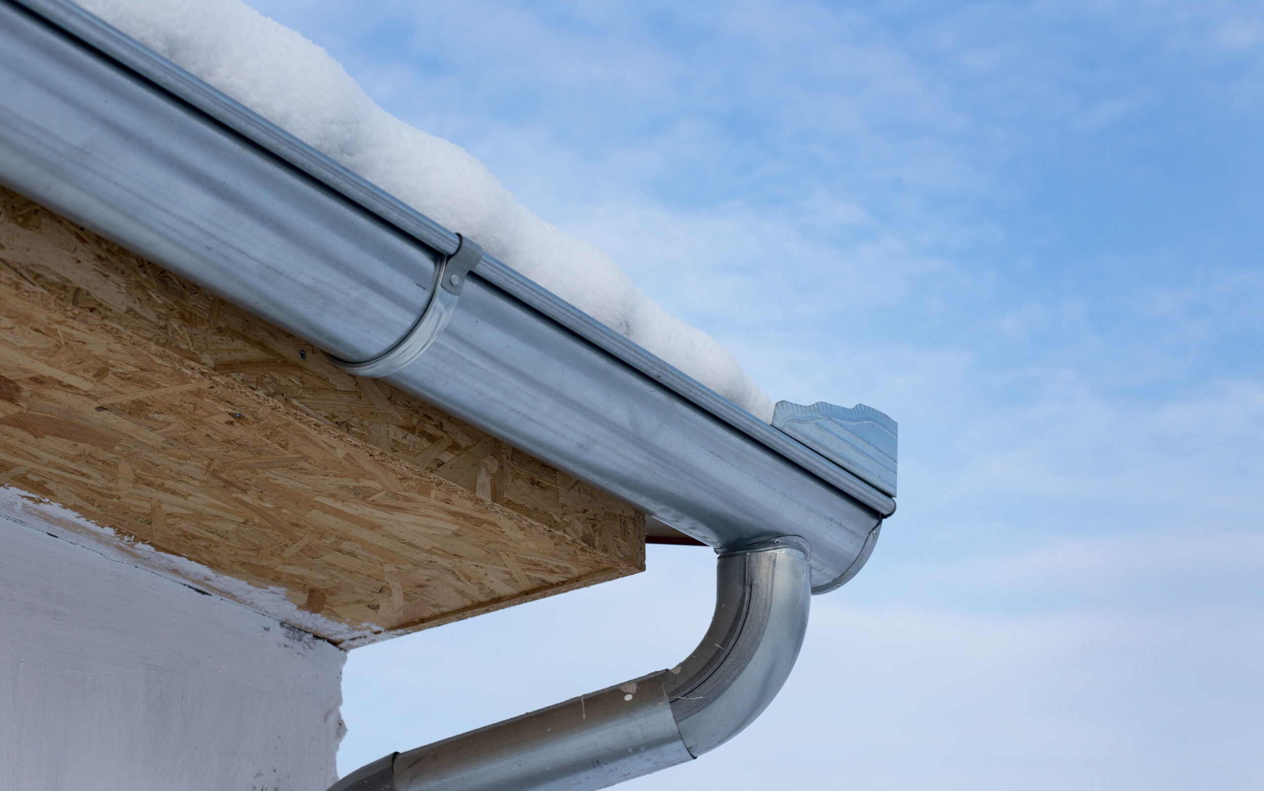 Close up of metal gutter on house with roof covered with snow