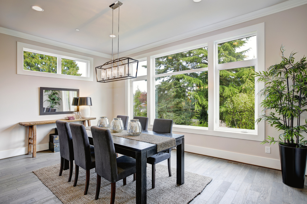 Luxurious modern dining room boasts a black dining table illuminated by a rectangular chandelier and surrounded by gray velvet dining chairs over taupe sisal rug finished with rustic console table.